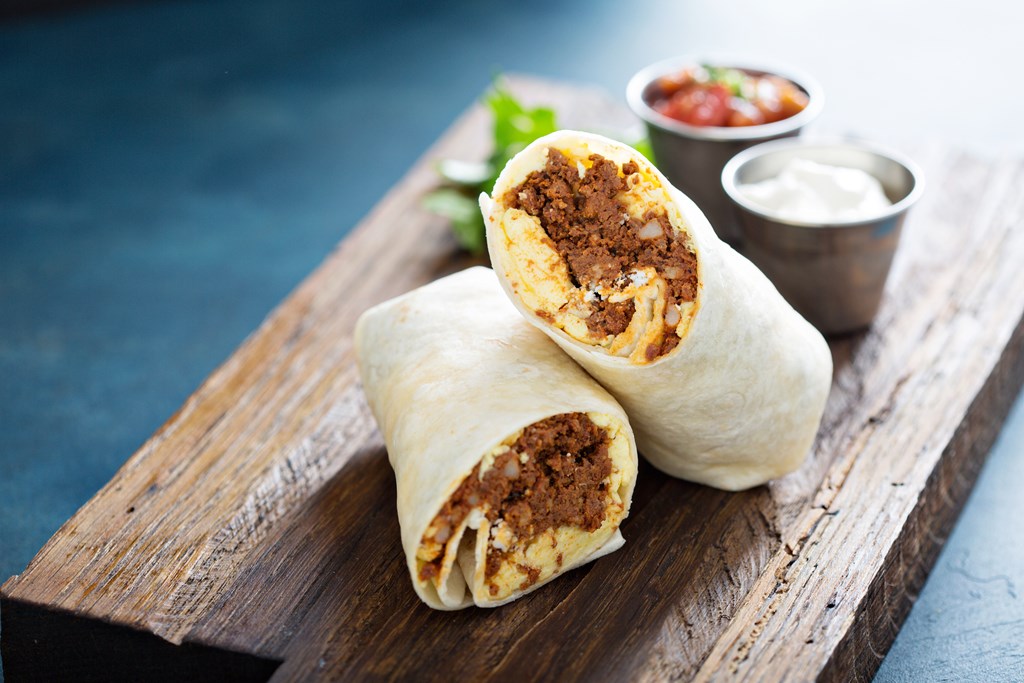 Breakfast burrito with spicy chorizo and egg on a cutting board.