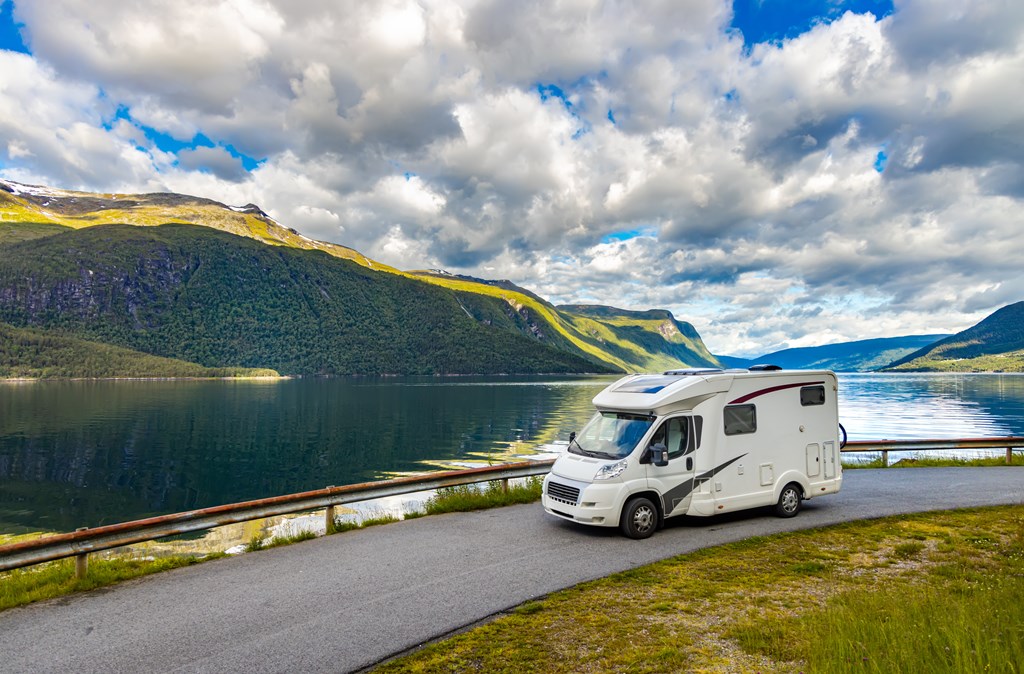 Small motorhome takes a road by a mountain lake.