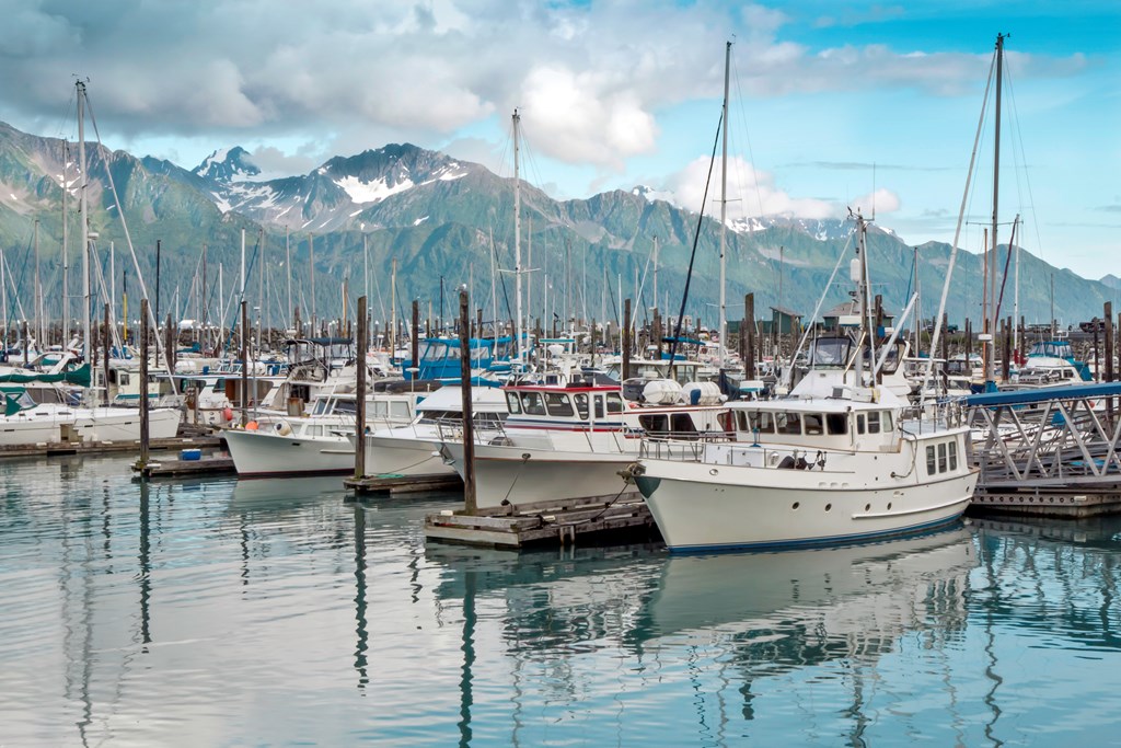 Fishing boats sit at piers in the harbor near Seward, Alaska. Snow-capped mountains appear in the background.
