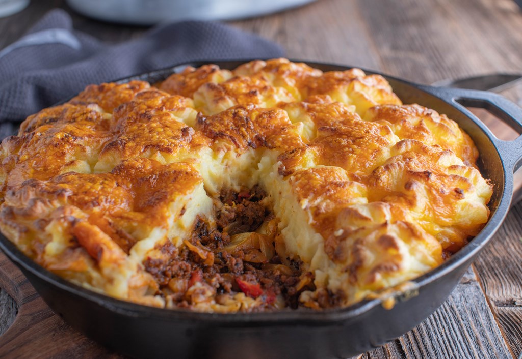 Delicious homemade cooked savory pie with ground beef, cabbage, vegetables and mashed potato, cheese crust. Served in a rustic cast iron pan on wooden table background.