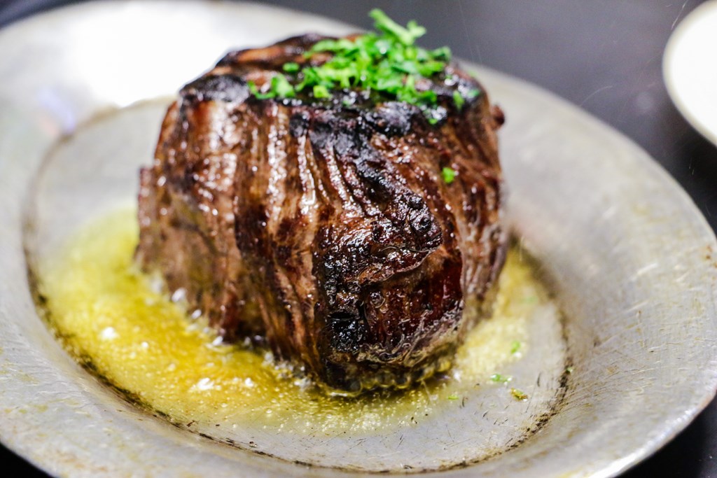 Filet mignon sizzling in butter on a silver serving plate.