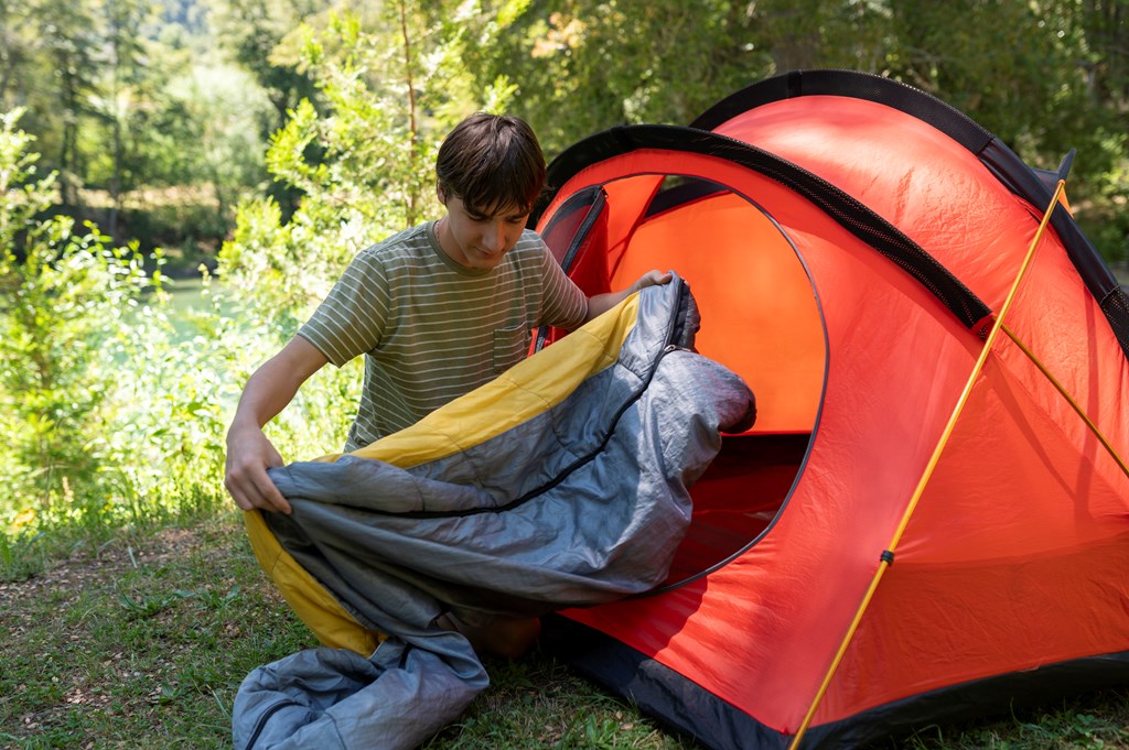 Young man preparing his tent and sleeping bag. 