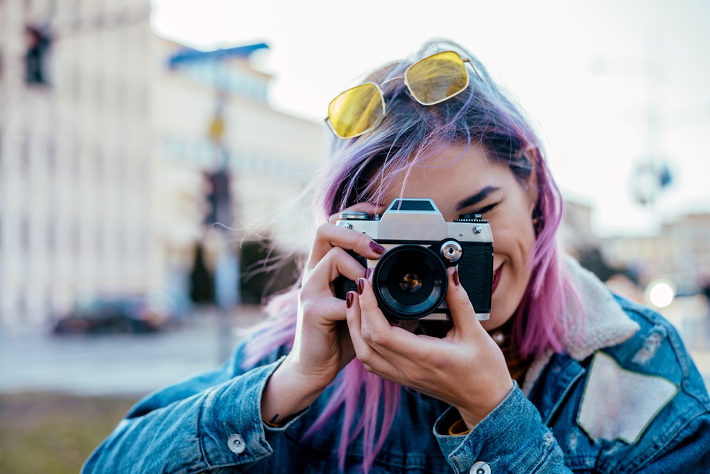 Close-up image of female photographer with pink hair using camera.