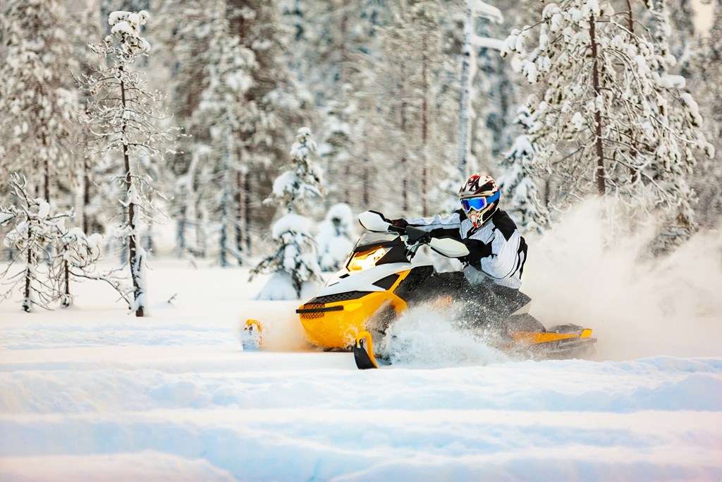 A person taking a turn on a yellow snowmobile in a snowy forest.