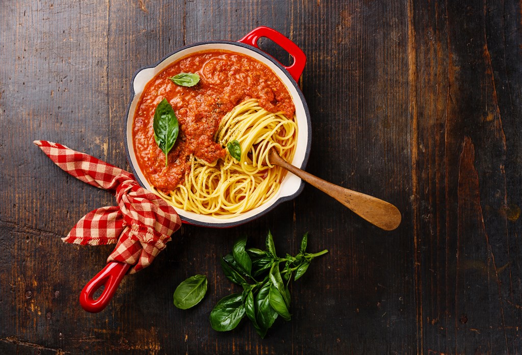 Spaghetti Bolognese with tomato sauce and basil in iron pan on wooden background.