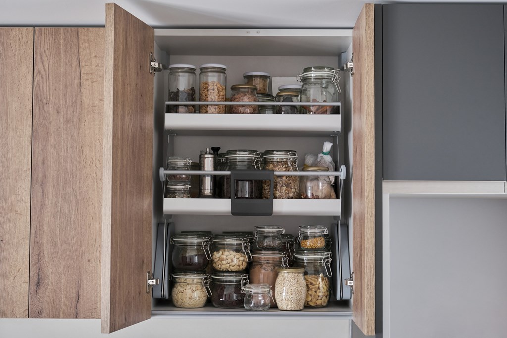 Variety of dry foods, grains, nuts, cereals in glass jars in kitchen cupboard. 