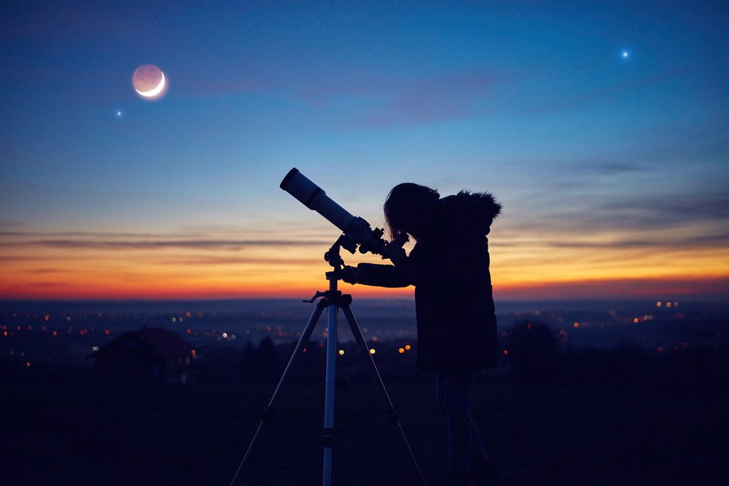 Child observing stars, planets, Moon and night sky with astronomical telescope.
