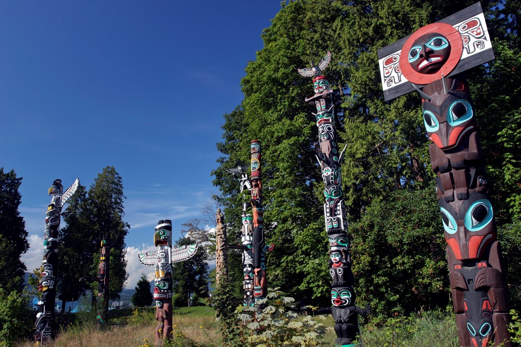 First Nations totem poles stand tall against a blue sky in Vancouver's Stanley Park.