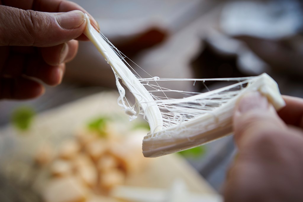 Close up of hands pulling string cheese apart.