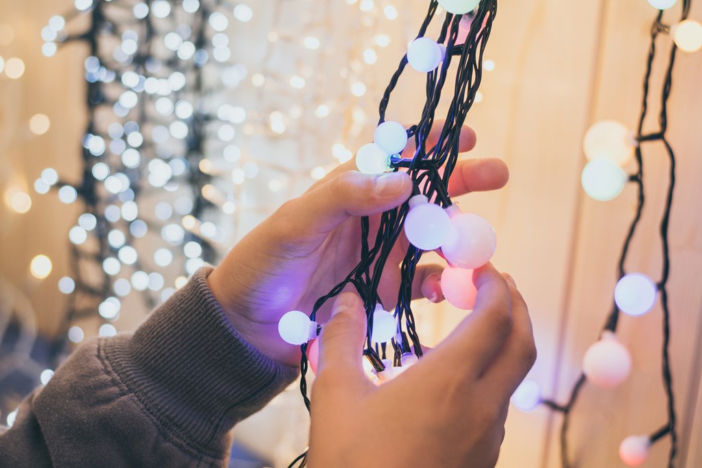 Closeup of young hands putting up string lights.