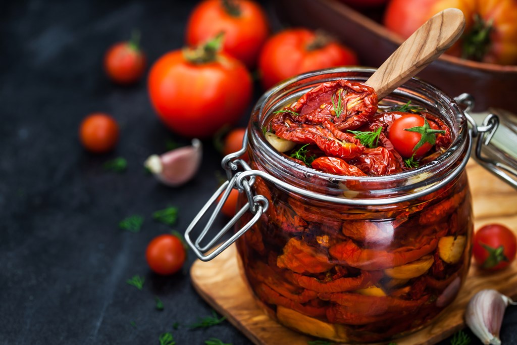 Sun dried tomatoes with garlic and olive oil in a jar on dark background.