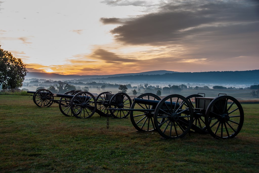 Sunrise and mist hang over antique cannons at Antietam National Battlefield.