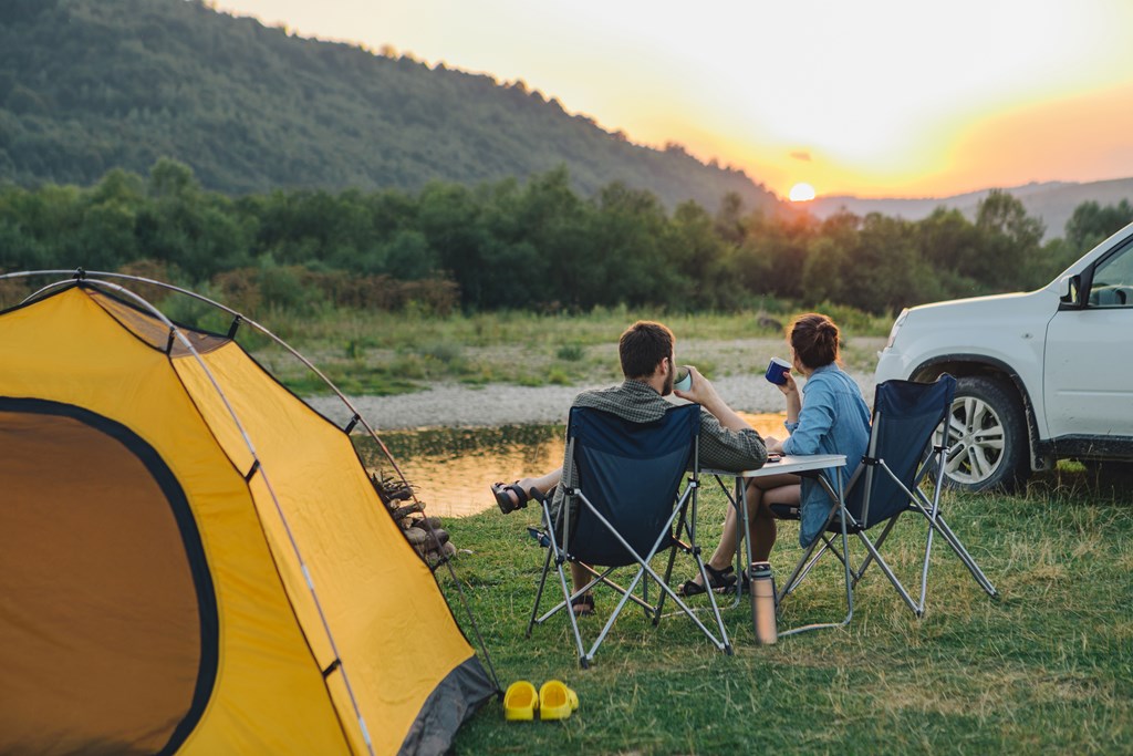 Couple sitting in camping chairs enjoying coffee while watching the sunset.