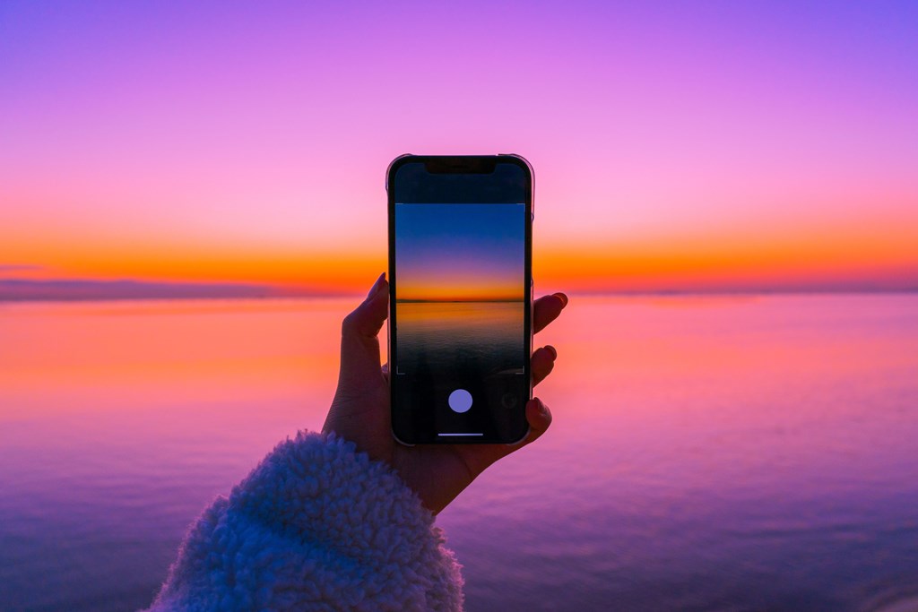 Cell phone taking a photo of water and sky at sunset.