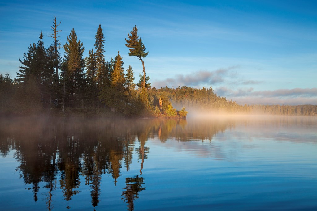 Blue Trout Lake and island in northern Minnesota with fog on the water at sunrise during September.