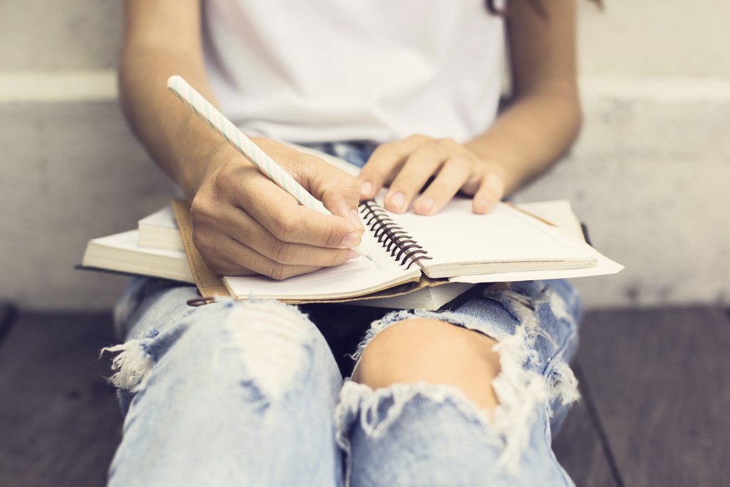 Closeup of a teenager writing in a notebook.