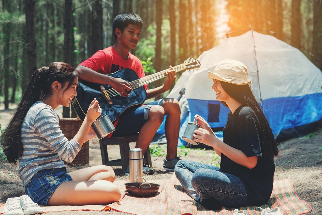 A group of three teenagers enjoy a camping trip by playing music.