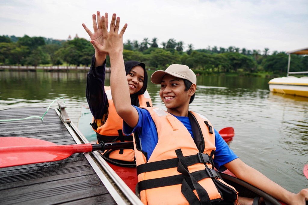 Two teen boys high five before pushing their kayak away form the dock.