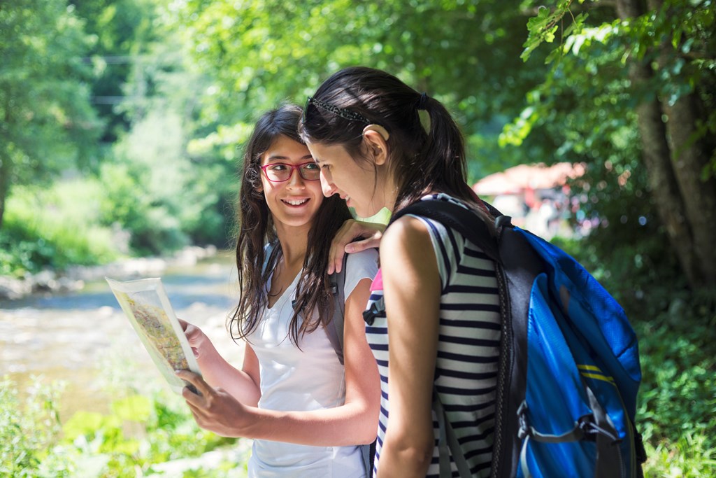 Two teen girls stop on their hike to look at a map.
