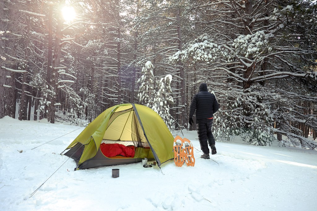 Man stands next to a green camping tent in the snow.