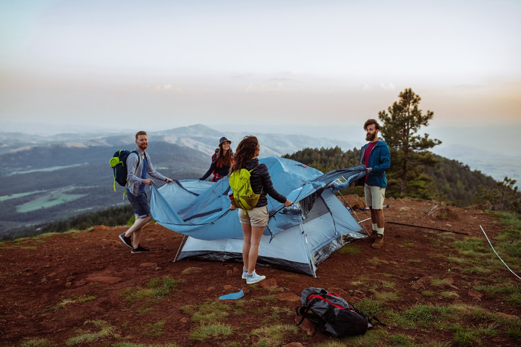 Four friends setting up their tent in the mountains by adding a rain fly.