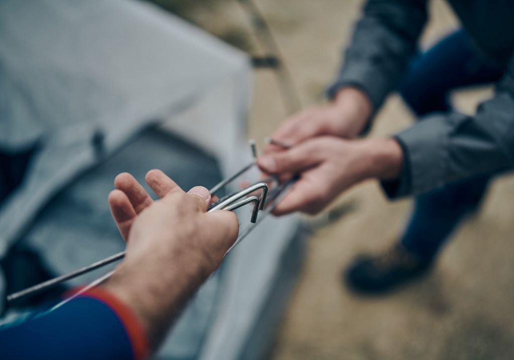 Closeup of two hikers hands grabbing tent ground steaks.
