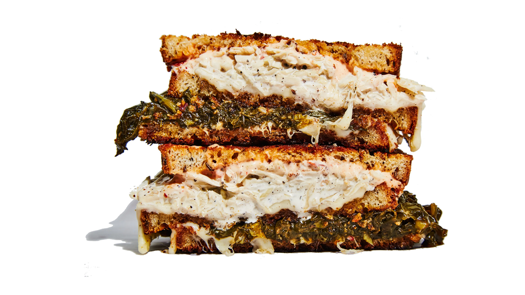 A sandwich on a white background piled high with collard greens and melty cheese.