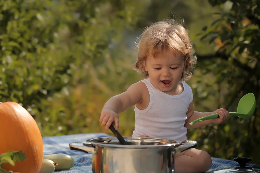Toddler playing with a cooking pot outdoors.