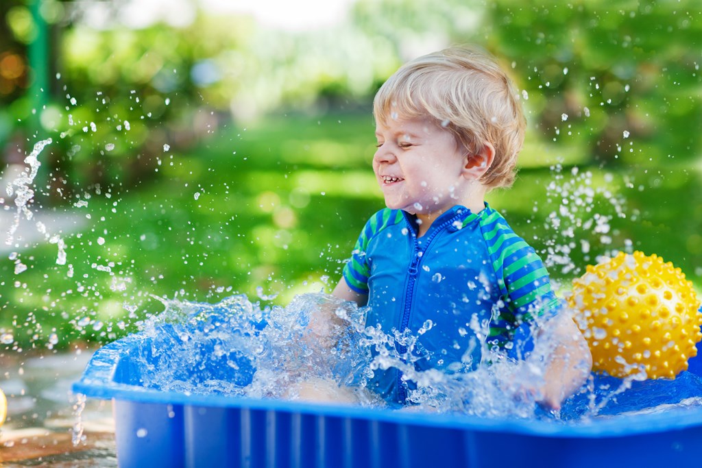 Little toddler boy having fun with splashing water in summer garden pool.
