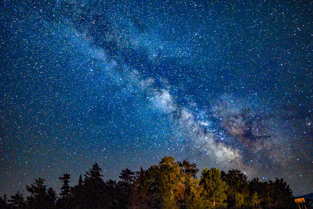 A stunning view of the Milky Way appears over the trees in the Adirondack Mountains near Tupper Lake.