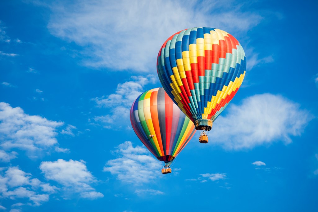 Two colorful hot air balloons flay against a blue sky with wispy clouds.