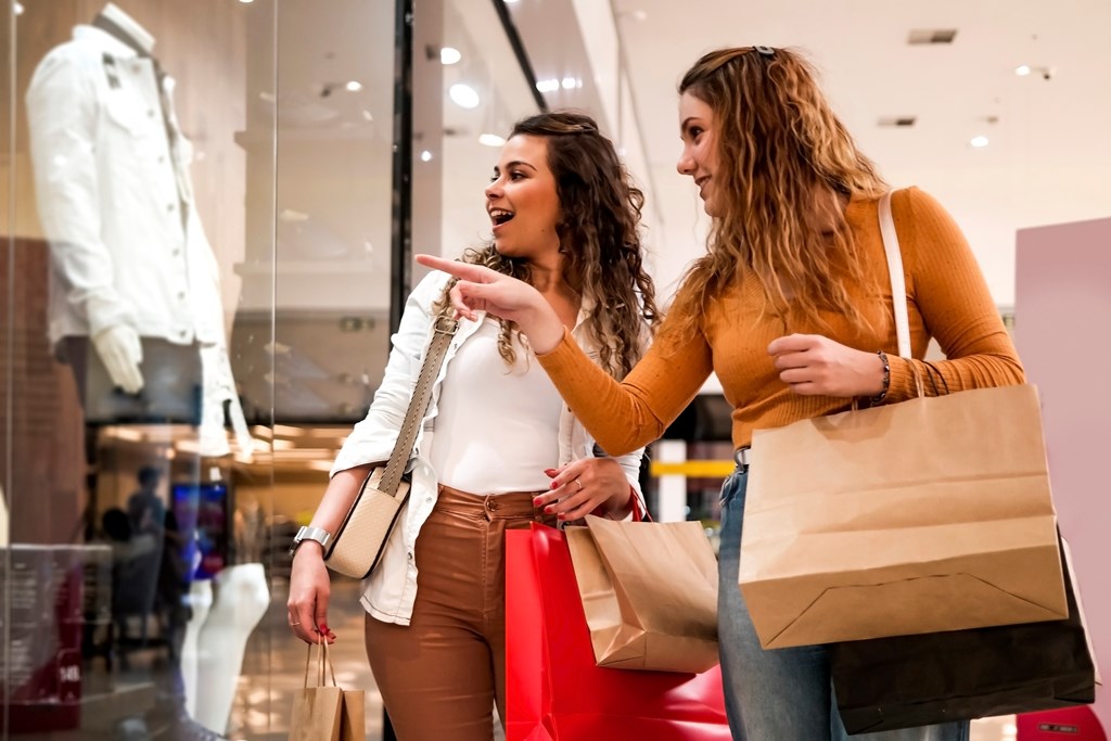 Two women shopping. One is pointing out something through the window of a store.