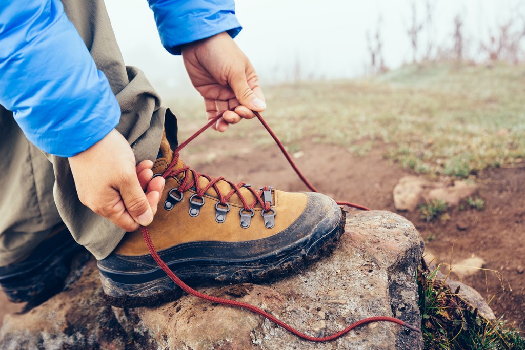 Hiker tying shoelace of hiking boot on foggy highland mountain.