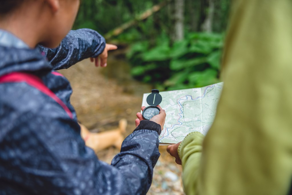 Daughter and mother hiking in forest using compass and map to navigate