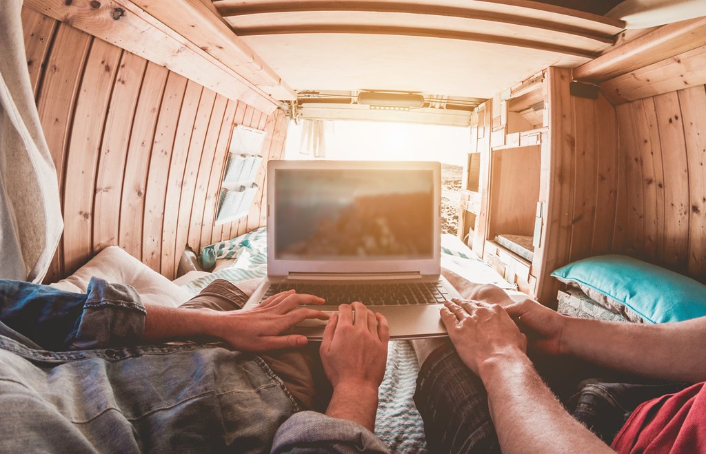 Digital nomad couple working inside a camper van with wood interior.