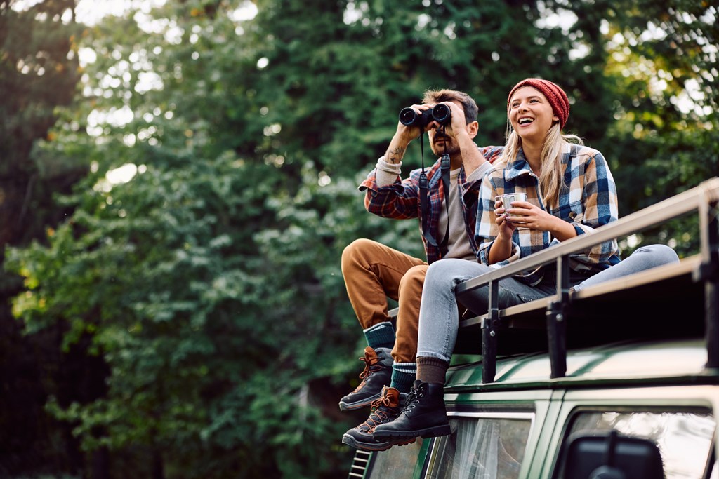 Woman and her boyfriend using binoculars while sitting on roof of their camper van.