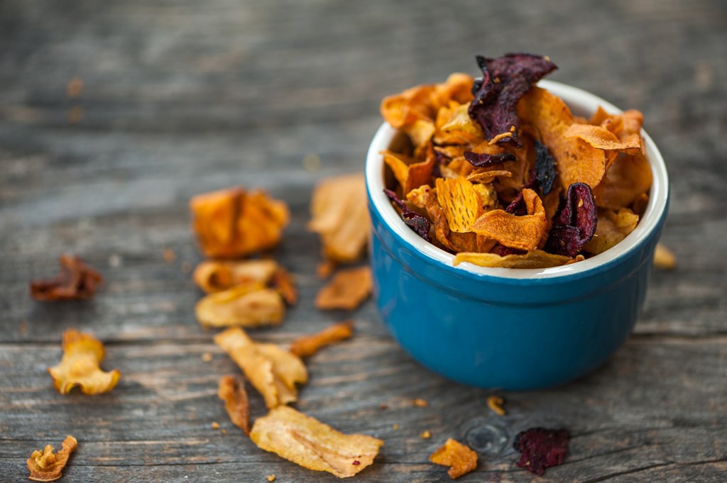 Close up of a blue bowl with vegetable chips on a rustic table.