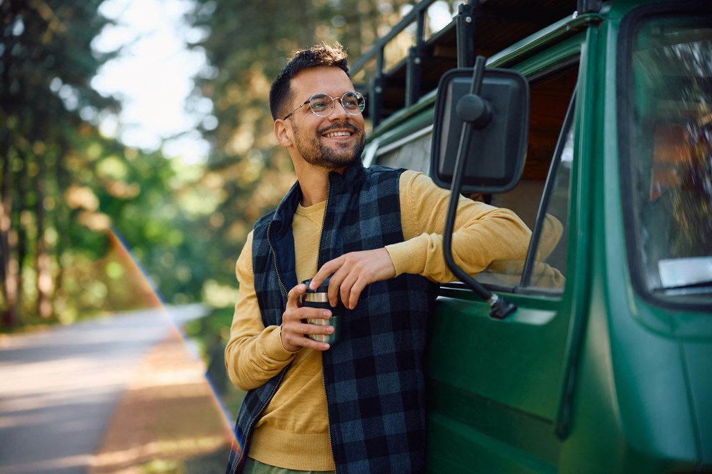 Happy camper having a cup of coffee by his travel van in nature.