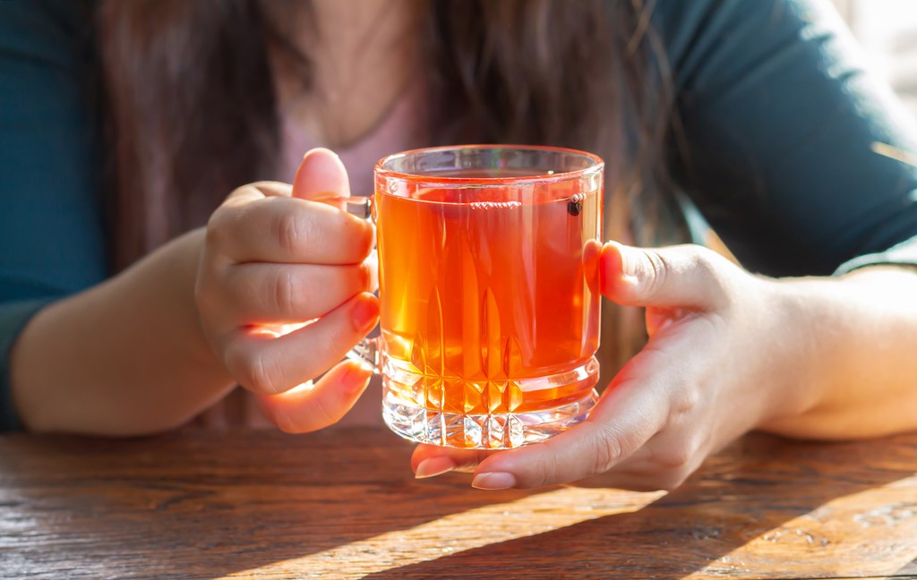 Female hand holding hot cup of fruit tea on sunny morning