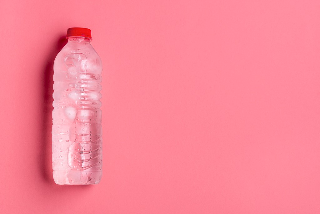 Cold water in a plastic bottle on a pink background. 