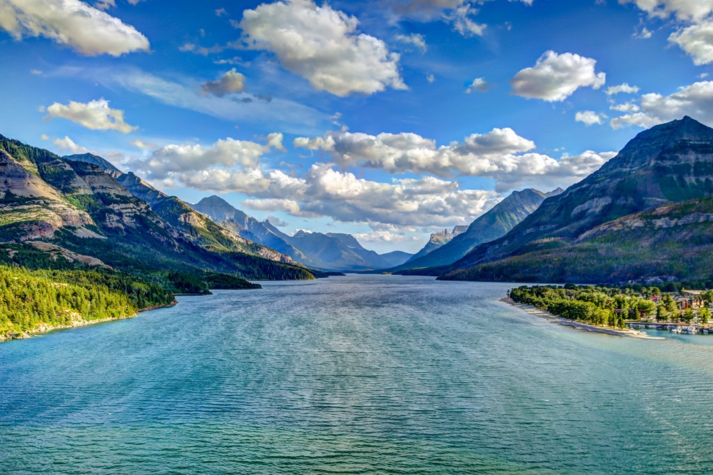 Waterton Lake surrounded by tall mountains under a blue sky with fluffy clouds.