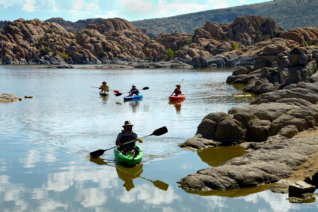A group of friends paddles kayaks in the shallows of rock-edged lake in Arizona.