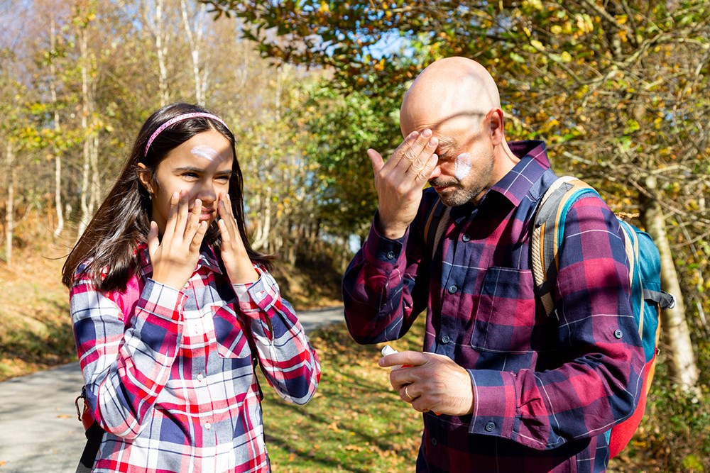 Father and teenage daughter applying sunscreen before hiking on a sunny autumn day.