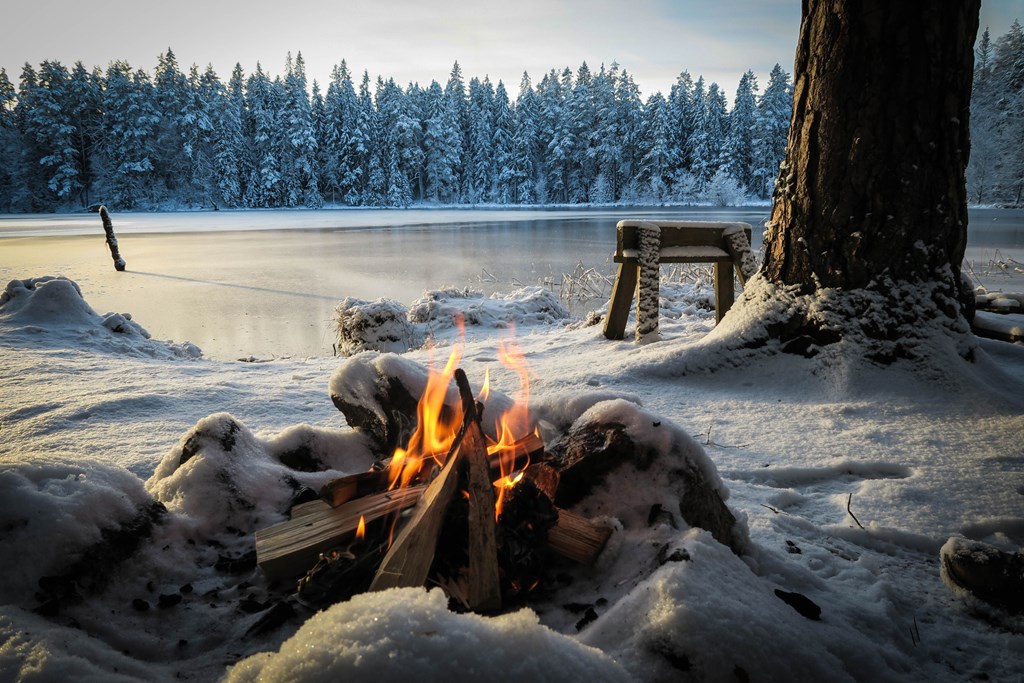 A campfire burns near a snowy and icy lake in winter.