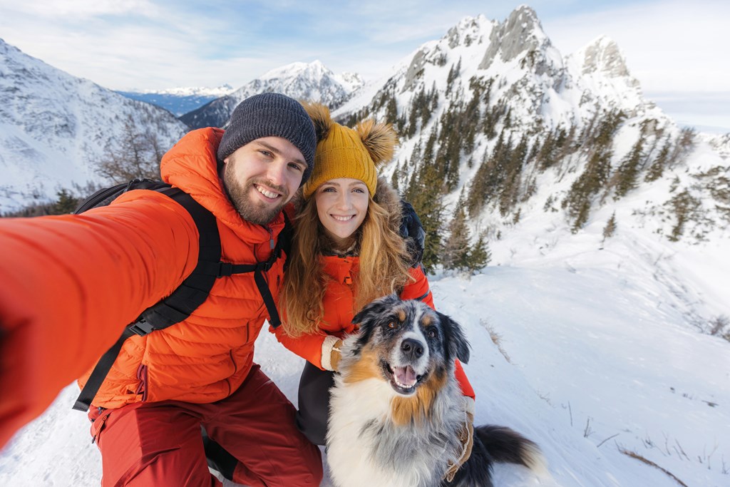 Hiker couple with a dog takes a selfie from a snowy landscape in the winter mountains.