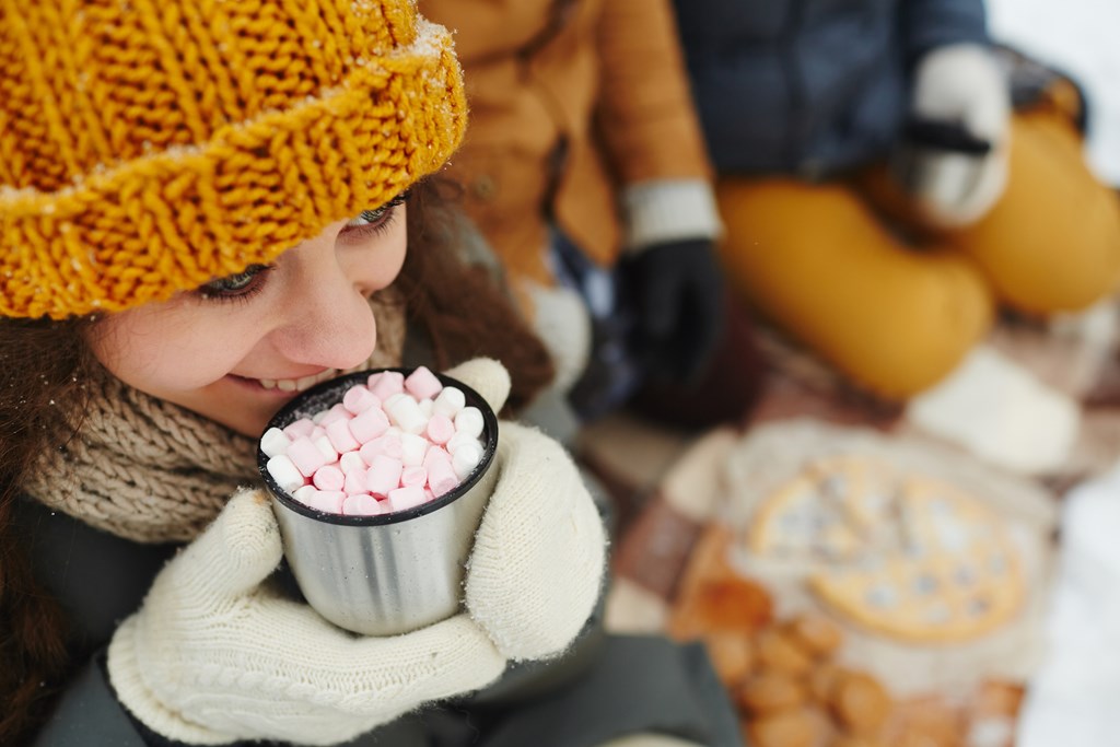 A woman smiles as she takes a sip of her hot cocoa with marshmallows on a winter day.