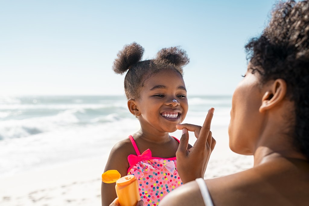 Young mother applying protective sunscreen on daughter nose at beach .