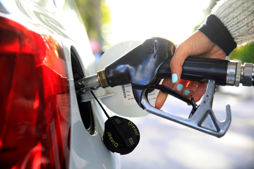 Close-up of a person with blue nail polish refueling at a gas station.