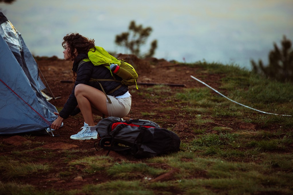 Shot of a young woman setting up a tent in the mountains.