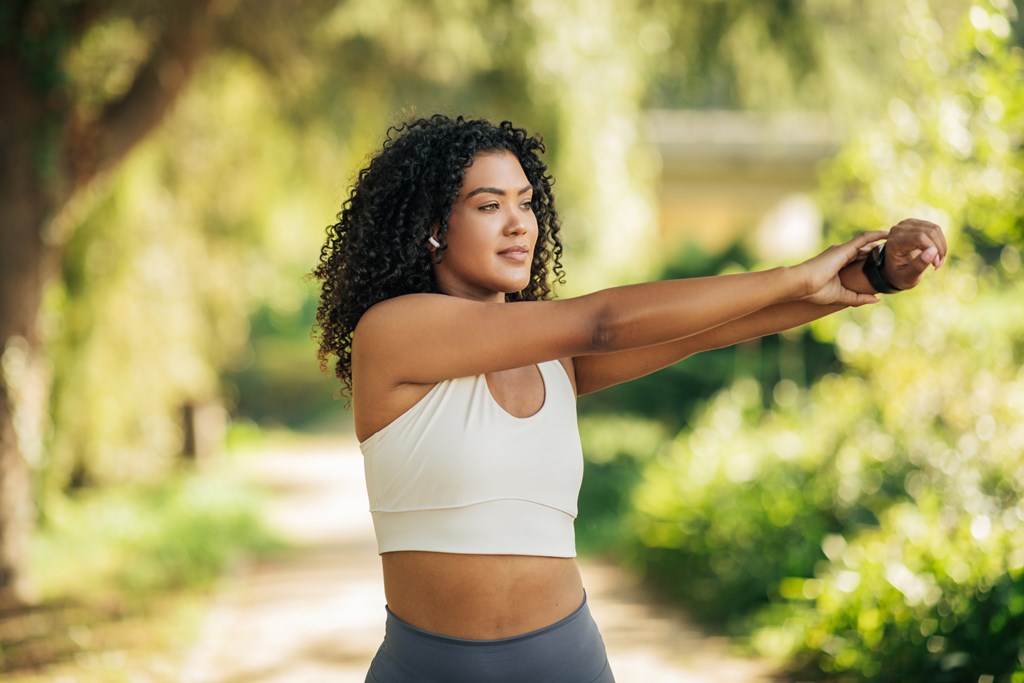A young woman wearing sportswear is seen exercising in a lush, sunny park during the afternoon.